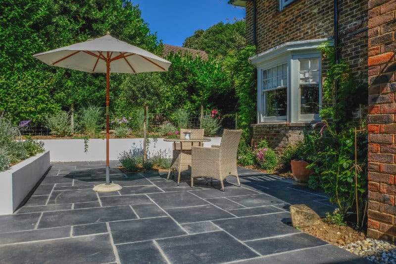 Table and chairs on the patio in an English country garden.  Taken on a sunny summer day with plants and flowers.